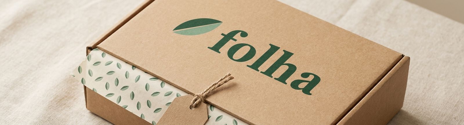 Closed Folha sample kit box in kraft corrugated board with the Folha logo, leaf-pattern tissue paper and a hang tag, on linen